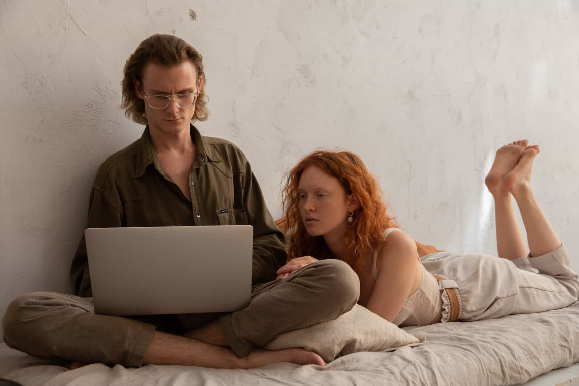 focused couple browsing laptop on bed
