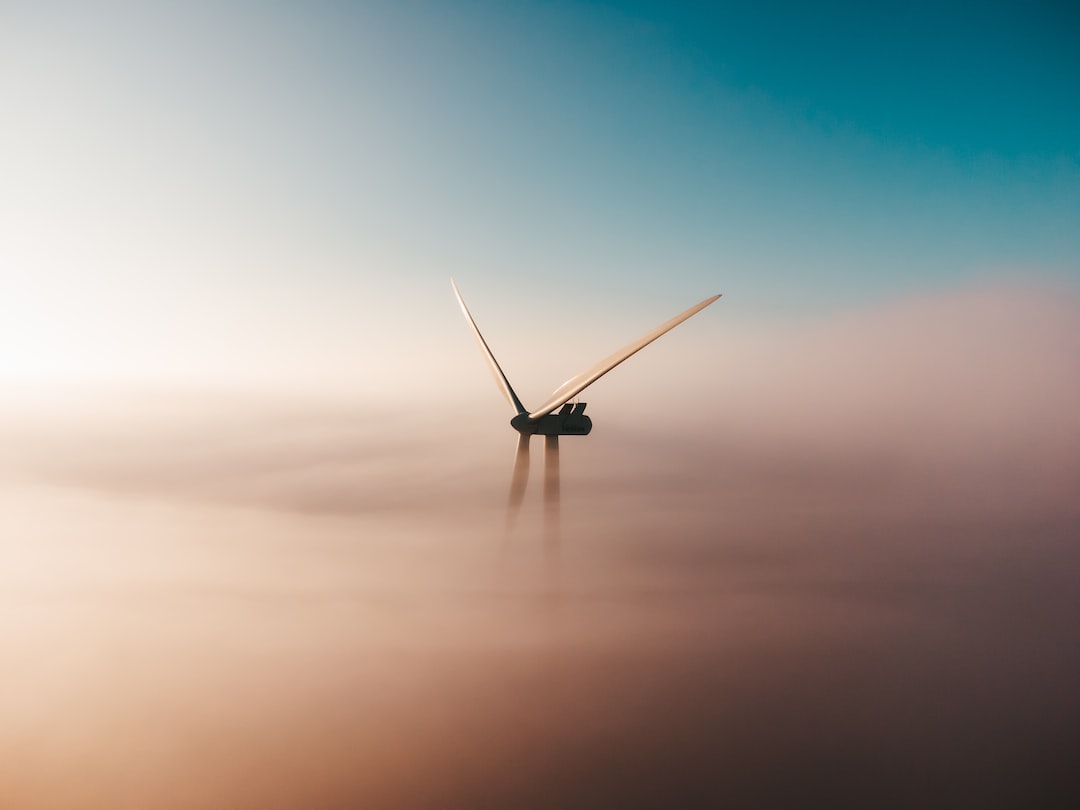 An image that showcases a close-up view of a wind turbine's blades, capturing their sleek, aerodynamic design as they effortlessly slice through the air, surrounded by a vibrant blue sky and a backdrop of rolling hills